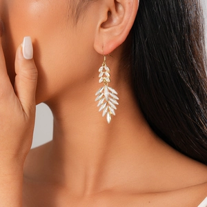 Elegant gold leaf earrings featuring sparkling white crystals worn by a model in soft light