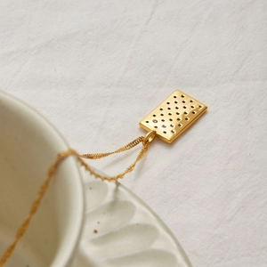 Gros plan d'un pendentif rectangulaire doré 18K avec points ajourés sur chaîne