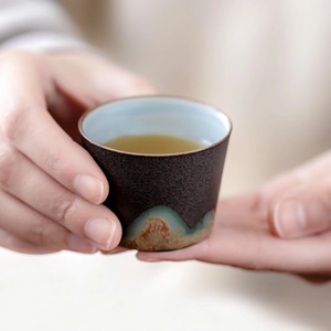 Ceramic tea cup with vintage mountain pattern and brown stoneware texture in hands