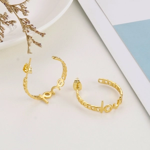 Detailed close-up of 18K gold-plated LOVE letter hoop earrings on a minimalist background