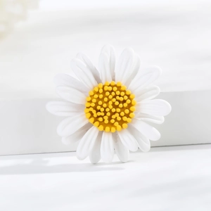 Delicate white daisy brooch with yellow center on minimalist surface