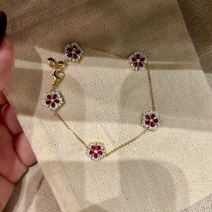Close-up of gold flower bracelet with red and white zircon stones on linen background