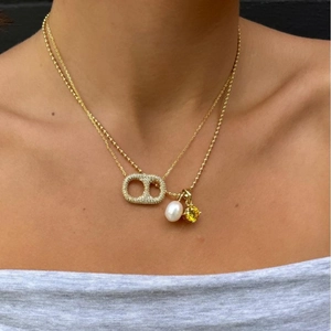 Double-layered gold necklace featuring a pearl and yellow gemstone pendant on a female model