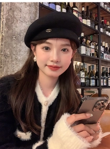 Detail of black wool beret with metal logo emblem on an elegant French style model