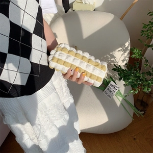 Detail of yellow striped bubble fabric cosmetic bag held by a model in soft sunlight