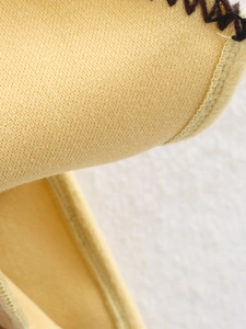Detailed macro view of yellow woolen fabric texture and fine stitching on the cape jacket