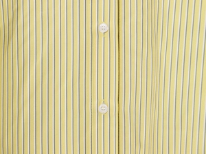 Detail of yellow striped shirt fabric featuring white buttons and precise stitching texture
