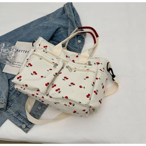 White canvas tote bag with cherry print, red handles, and detachable strap on denim background