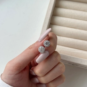 Close-up of S925 sterling silver halo stud earrings held by a model with a soft background