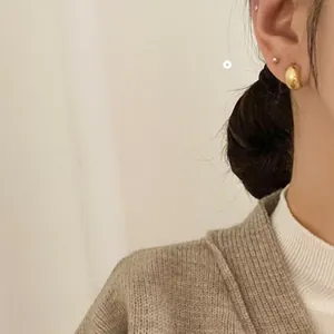 Close-up of minimalist golden dome earrings worn by a model in a cozy, elegant setting