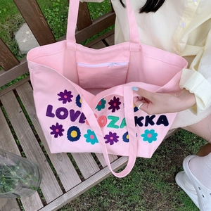 Detail of pink canvas tote bag featuring floral embroidery and internal zipper pocket