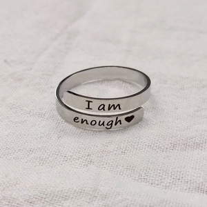 Macro detail of 'I am enough' engraved adjustable stainless steel wrap ring on white fabric
