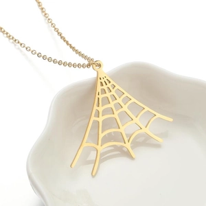 Detailed view of a gold spider web pendant necklace resting in a white ceramic bowl
