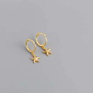 Macro detail of gold starfish pendant earrings with detailed texture on grey background