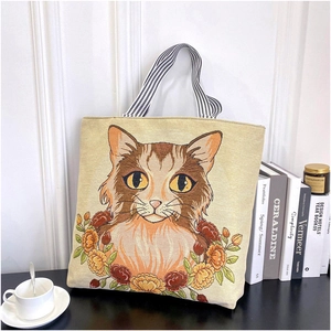 Detail of embroidered cat and floral canvas tote bag with books and coffee setup
