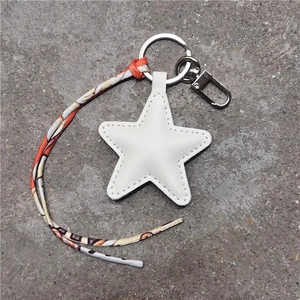 Close-up of a white star-shaped leather keychain with colorful silk ribbon and metal ring