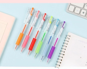 Close-up of 6 colorful retractable gel pens on a desk with a white keyboard and notepad