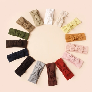 Flat lay of 14 colorful ribbed baby bow headbands arranged in a circle on beige background