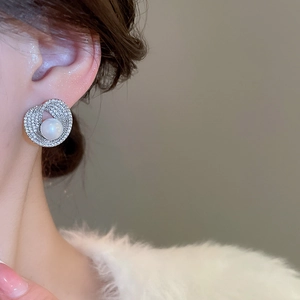 Close-up of elegant pearl earrings with pavé rhinestones worn by a model in soft light
