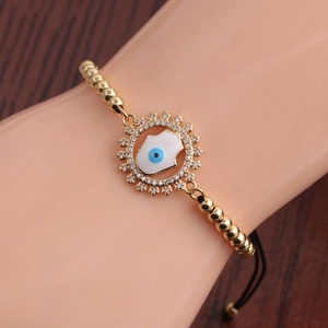 Détail macro du bracelet à perles dorées avec main de Hamsa et œil de zircon sur un poignet