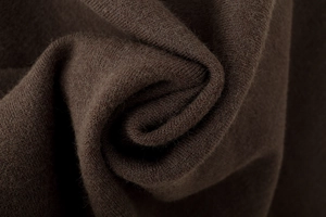 Makro-Detail von dunkelbraunem Poncho-Strickstoff mit weicher Spiralkonstruktion und Textur