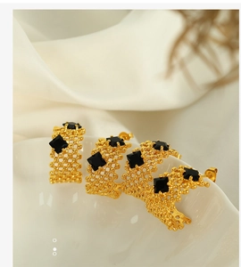 Détail de boucles d'oreilles C plaquées or 18K avec pierre noire sur fond de soie