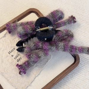 Detailed close-up of purple knitted wool bow hair claw clip on wooden tray