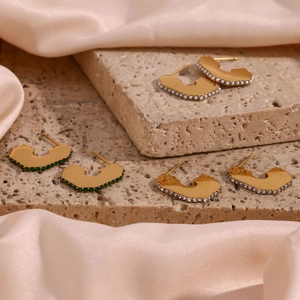 Detailed close-up of golden geometric earrings with white pearl and green zircon details