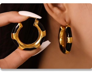 Macro detail of gold hoop earrings with black enamel pattern and chunky textured surface