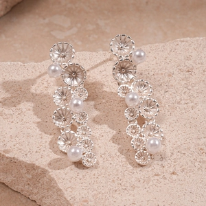 Detail of silver daisy flower drop earrings with white pearls on a natural stone surface