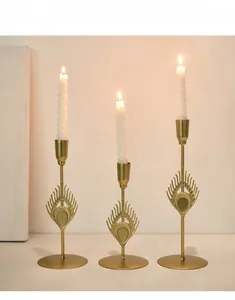 Detailed view of three golden peacock feather metal candle holders with white spiral candles