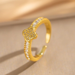 Gold-plated four-leaf clover open bangle with zircon crystals on warm gold fabric