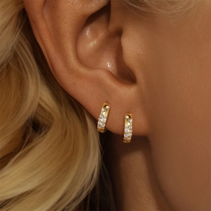 Close-up of golden hoop earrings with pavé set white zirconias worn by a model