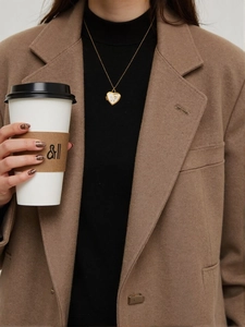 Close-up of gold heart locket necklace with LOVE engraving worn on a brown coat