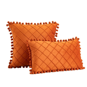 Orange velvet throw pillows with diamond quilting and decorative pom poms on white background