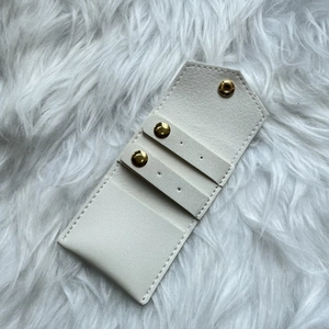 Portable white leather jewelry pouch with gold snaps on soft faux fur background