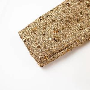 Dettaglio ravvicinato del tessuto tweed dorato con paillettes sul polsino della giacca