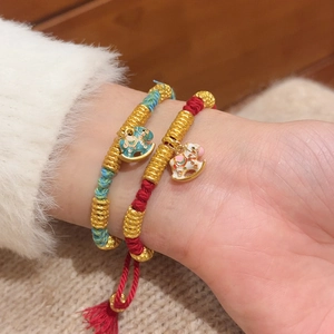Detail of red and blue braided bracelets with gold beads and enamel rocking horse charms