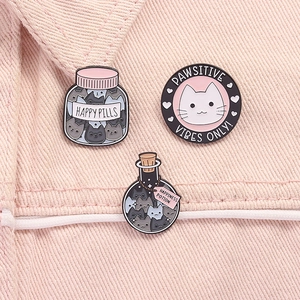Three cute enamel pins featuring cat designs on pink denim fabric background