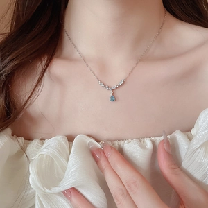Close-up of a silver chain necklace with a blue teardrop pendant worn on a female neck