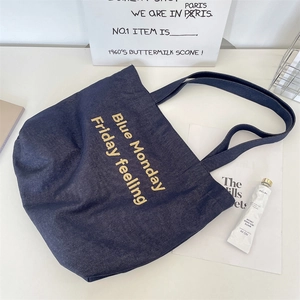Top view of a blue denim tote bag with yellow embroidery on a clean lifestyle background