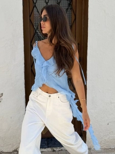 Detail of light blue ruffled sleeveless top with V-neck and white wide-leg trousers