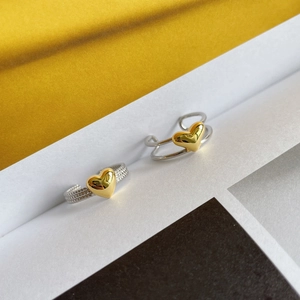 Macro shot of gold heart-shaped charms on twisted silver rings over a geometric background