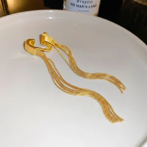 Elegant gold fringe ear bone clip with metallic tassels on a white ceramic tray