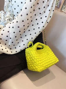 Neon yellow woven mini bucket bag held by a model in a stylish casual outfit