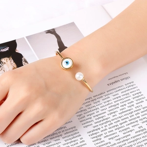 Detailed view of evil eye and pearl open cuff bracelet in 18K gold plated titanium steel