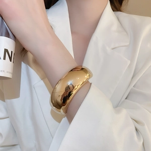 Bracelet large en métal doré poli sur mannequin portant un blazer blanc élégant