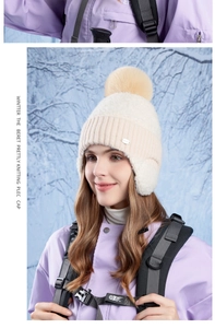 Close-up of thick beige knit texture with a fluffy pom-pom and metal logo detail