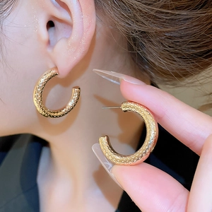 Detail of gold C-shaped hoop earrings featuring a vintage hammered textured surface finish