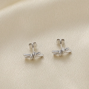 Elegant silver knotted stud earrings on champagne silk fabric background for women